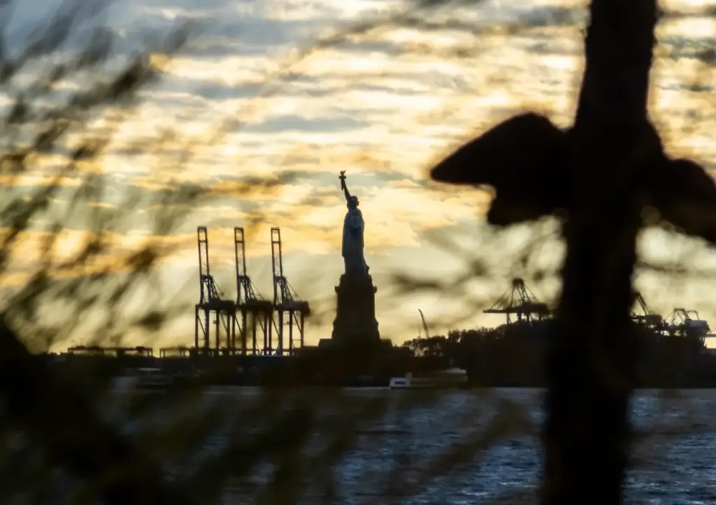 Statue of Liberty at sunset with harbor cranes behind it